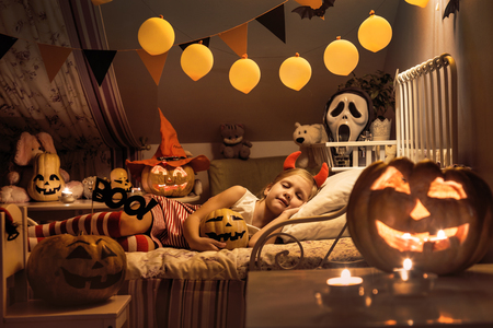 Little girl is sleeping in a children's bedroom decorated for Halloweenの写真素材
