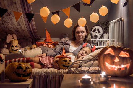 Mom looks at the sleeping daughter in  children's bedroom decorated for Halloweenの写真素材