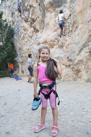 little girl in climbing equipment with a rope on the background of climbing tracksの写真素材