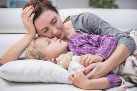 caring mother hugs her young daughter asleep from the disease at homeの写真素材
