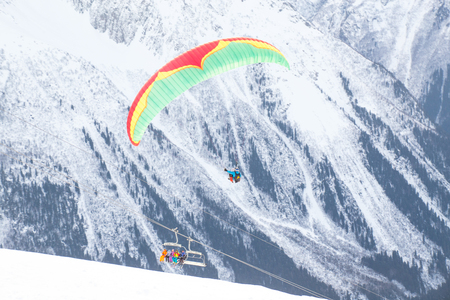 paraglider with two people - an instructor and a passenger flying the sky in the snowy mountainsの写真素材