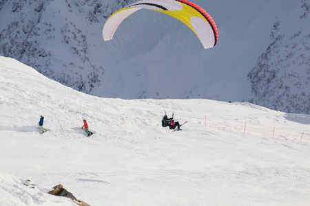 paraglider with two people - an instructor and a passenger flying the sky in the snowy mountainsの写真素材