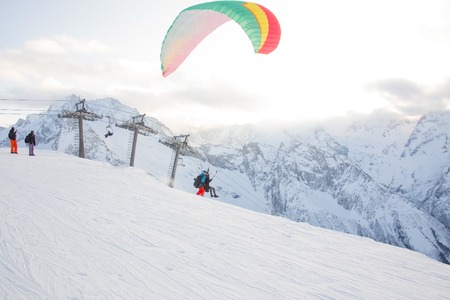paraglider with two people - an instructor and a passenger flying the sky in the snowy mountainsの写真素材