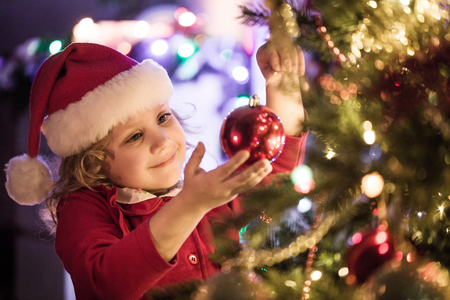 Little girl in Santa hat decorates a Christmas treeの写真素材