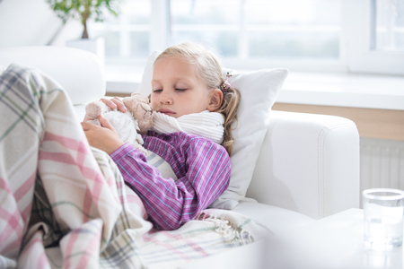 little girl is sick and lies at home on the couchの写真素材