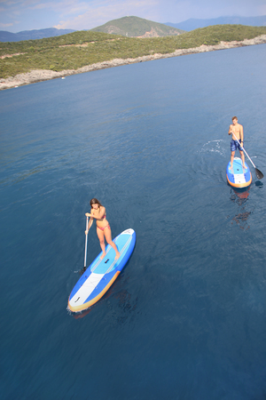 young people in swimming suit riding  on sup surfing in the seaの写真素材