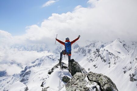 mountaineer with ice ax stands on the top of a mountain in the background of the landscape of snowy mountainsの写真素材