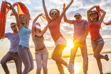 group of happy young people dancing at the beach on  beautiful summer sunsetの写真素材