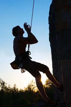 Silhouettes of  man climbing on a cliff at sunsetの写真素材