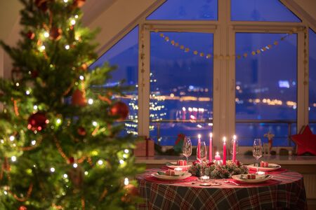 beautifully decorated Christmas table with candles and glasses near the Christmas treeの写真素材