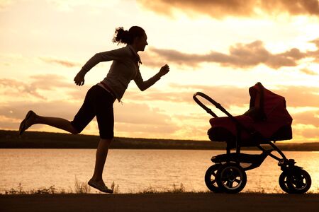 young mother is running to stroller with a baby at sunsetの写真素材