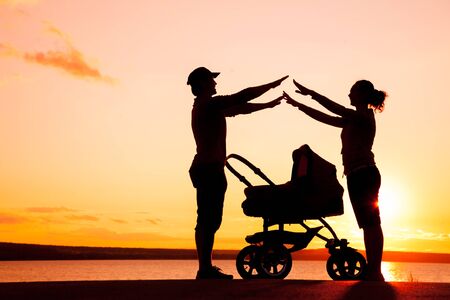 Silhouettes of young parents loving  their baby in a strollerの写真素材