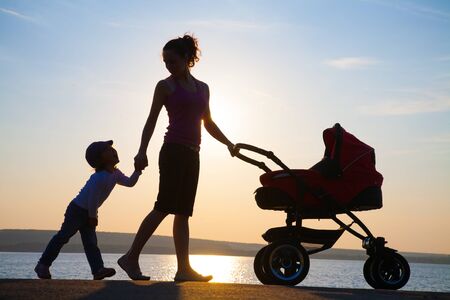 silhouette of a young mother walkes with  baby in a stroller at sunsetの写真素材