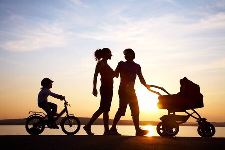 Silhouettes of young parents walking with children and  stroller on sunsetの写真素材