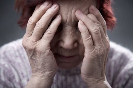 very old woman covered her face with wrinkled hands and is sadの写真素材