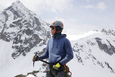 mountaineer with ice ax stands on the top of a mountain in the background of the landscape of snowy mountainsの写真素材
