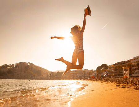 young happiness woman  jumping on sea beach against sun at sunsetの写真素材