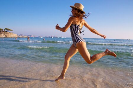 beautiful young woman in bikini runs along the sandy seashoreの写真素材