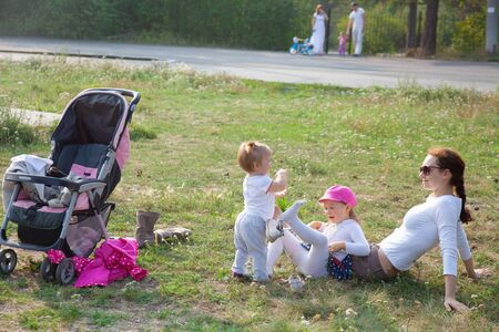 young mother sits with two  little daughter in park at summer dayの写真素材