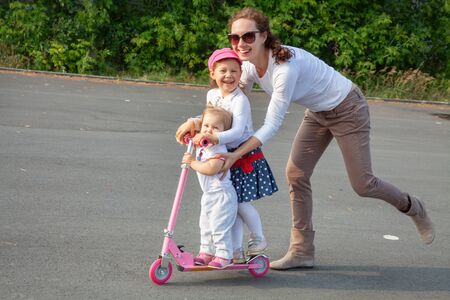 young mother skates with two  little daughter in park at summer dayの写真素材