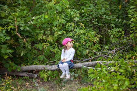 little girl sitting alone in a forest on a logの写真素材