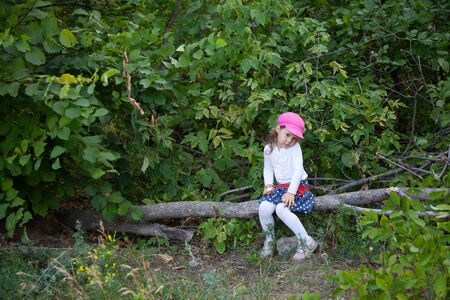 little girl sitting alone in a forest on a logの写真素材