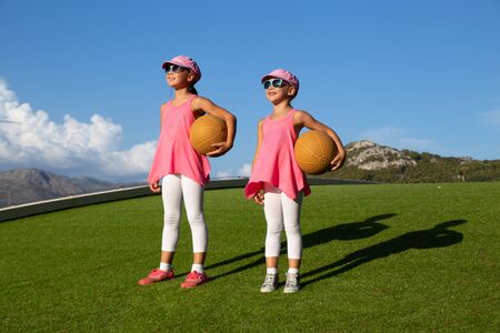 two little sporty girls perform fitness exercises on a green grass lawnの写真素材