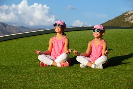 two little sporty girls perform fitness exercises on a green grass lawnの写真素材