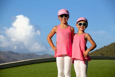 two little sporty girls perform fitness exercises on a green grass lawnの写真素材