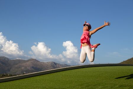 Cute girl jumping on summer meadow against blue skyの写真素材