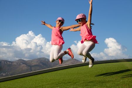 Little girls jumping on summer meadow against blue skyの写真素材