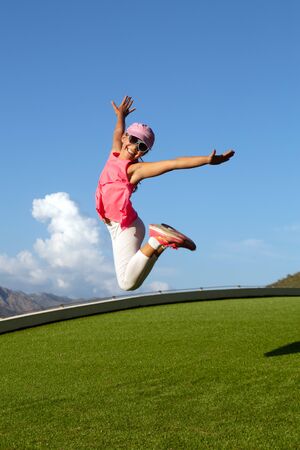 Little girl jumping on summer meadow against blue skyの写真素材
