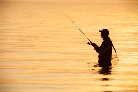 unrecognizable silhouette of man fishing at sunsetの写真素材