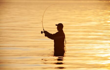 unrecognizable silhouette of man fishing at sunsetの写真素材