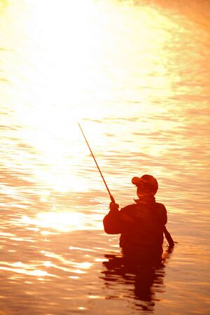 unrecognizable silhouette of man fishing at sunsetの写真素材