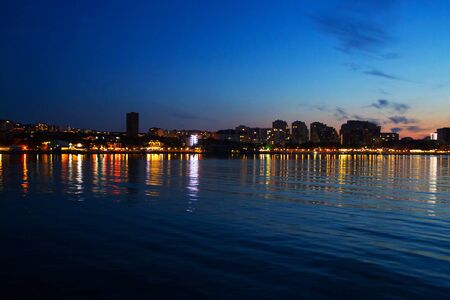 amazing colorful sunset on the sea coast with reflection of city lights in the waterの写真素材
