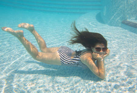 Cheerful little girl swiming under water in pool.の写真素材