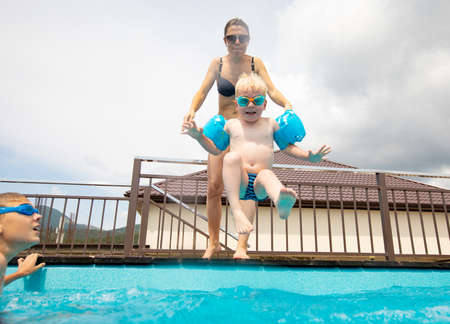young mother with little son jumping to swimming poolの写真素材
