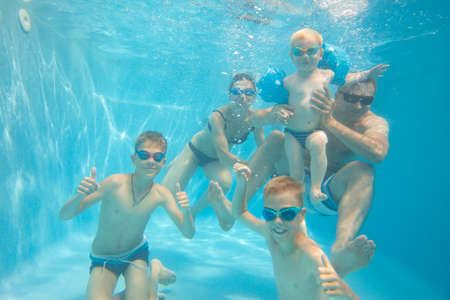 underwater photo of big young family with kids in swimming pool