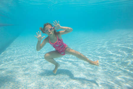 Cheerful little girl swiming under water in pool.の写真素材