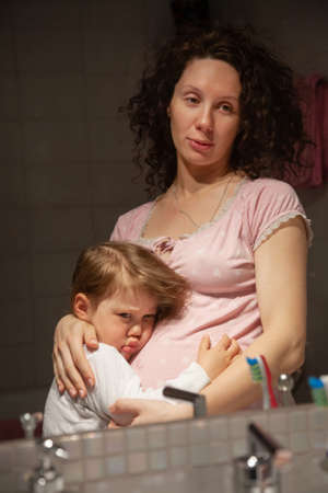 amateur portrait of a pregnant woman with a little baby through the bathroom mirrorの写真素材