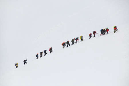 group of mountaineers with backpacks goes along the snowy slope of the mountainの写真素材