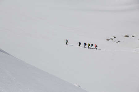 group of mountaineers with backpacks goes along the snowy slope of the mountainの写真素材