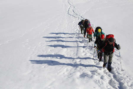 group of mountaineers with backpacks goes along the snowy slope of the mountainの写真素材