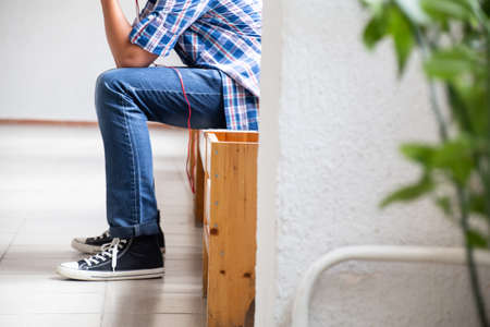Legs of a teenager sitting on a bench at school. Jeans and sneakers. Stress, crisis.の写真素材