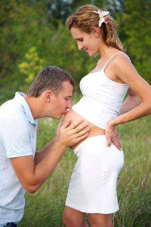 happy pregnant woman and her husband embracing her abdomenの写真素材