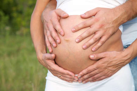 Hands of pregnant woman and her husband embracing her abdomenの写真素材