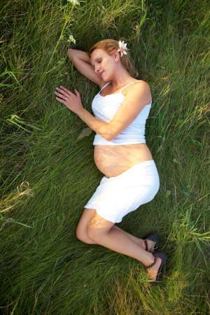 happy pregnant young woman lying in green grassの写真素材