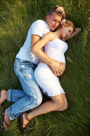 Man and pregnant woman sleeping together on grassの写真素材