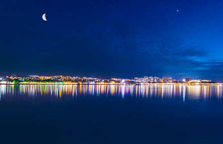 amazing colorful night photot of the sea coast with reflection of city lights in the waterの写真素材